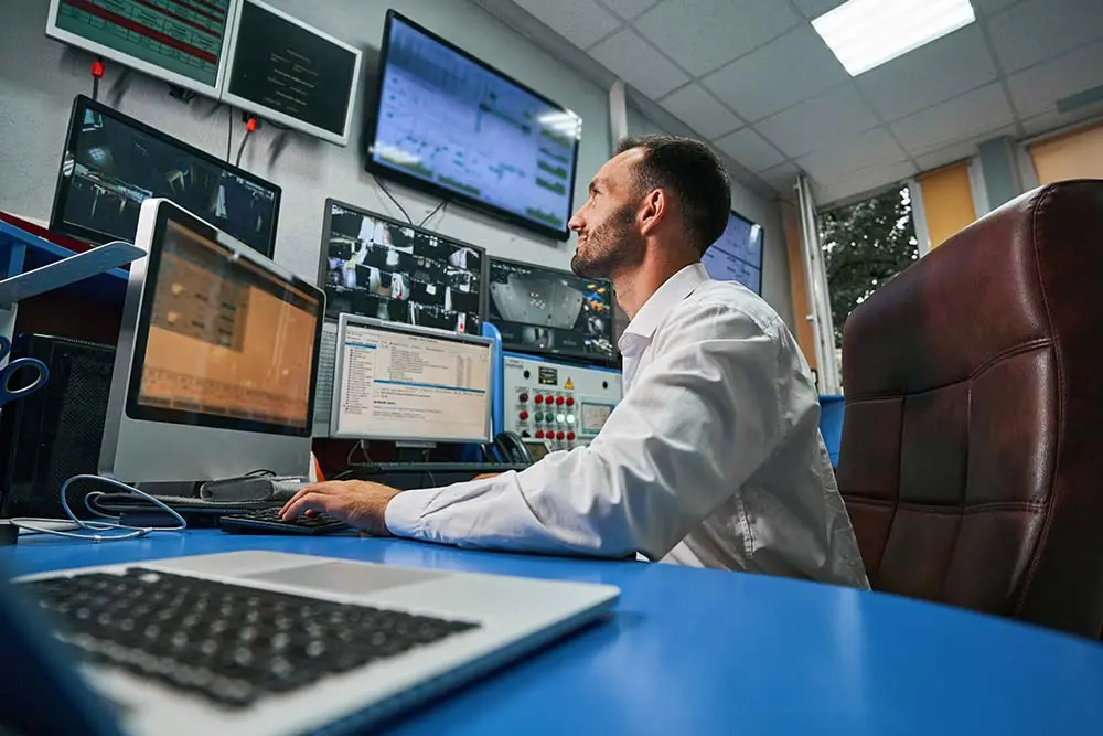 man looking at several monitors at desk